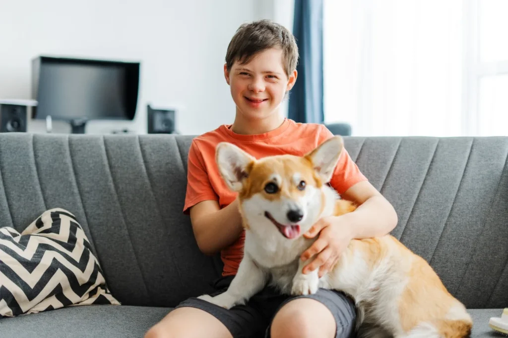 Disabled boy with down syndrome sitting on couch with Corgie dog