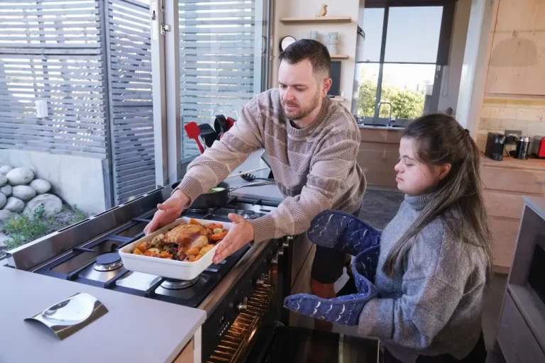 Support worker cooking roast chicken with disabled girl with down syndrome in kitchen